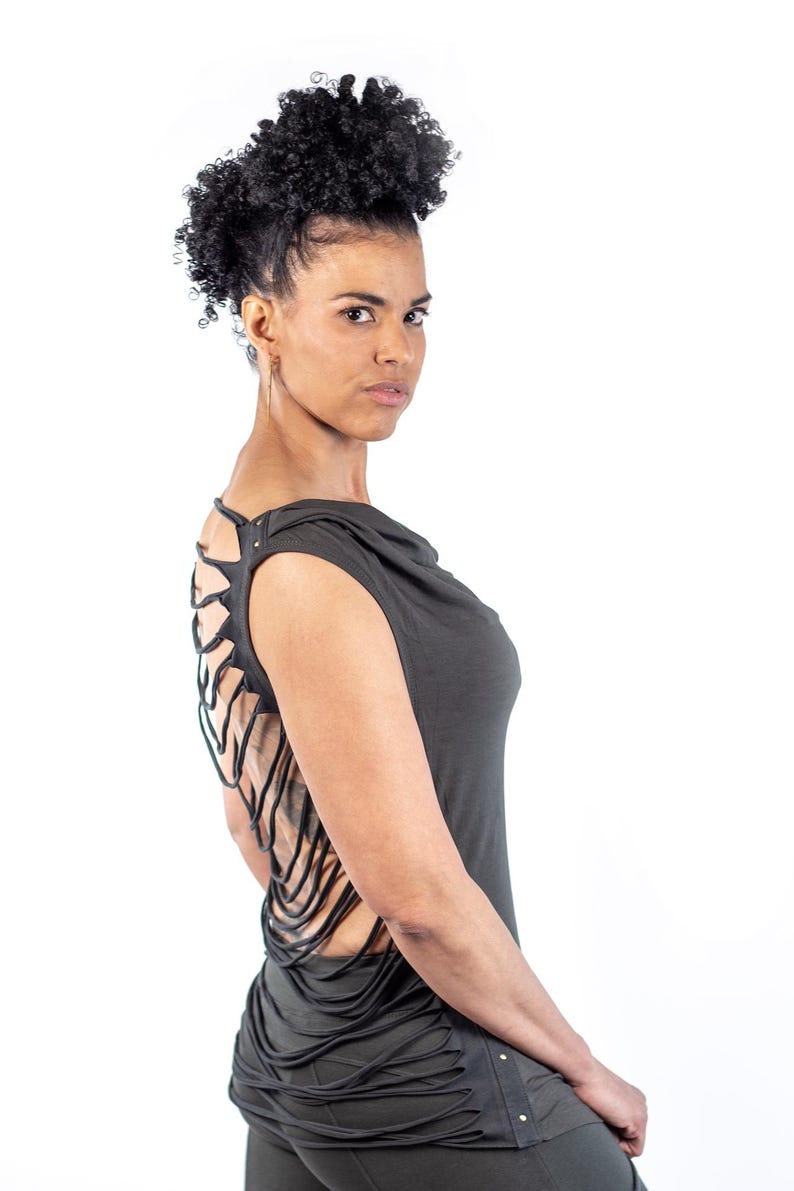May include: A woman wearing a dark gray sleeveless top with a unique cut-out design on the back. The top has a cowl neck and a relaxed fit.