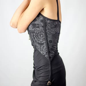 May include: Black dress with a decorative gray panel featuring a sun and moon pattern. The dress has thin straps and a fitted bodice that flows into a skirt. A gold-colored clasp accents the side.