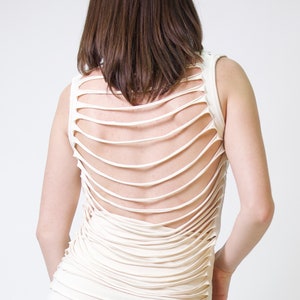 May include: A white sleeveless top with a unique design featuring multiple horizontal cutouts on the back.