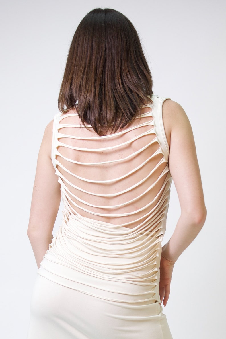 May include: A white sleeveless top with a unique design featuring multiple horizontal cutouts on the back.