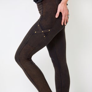 May include: Brown leggings with a decorative panel on the left thigh featuring a criss-cross design and gold-toned studs.