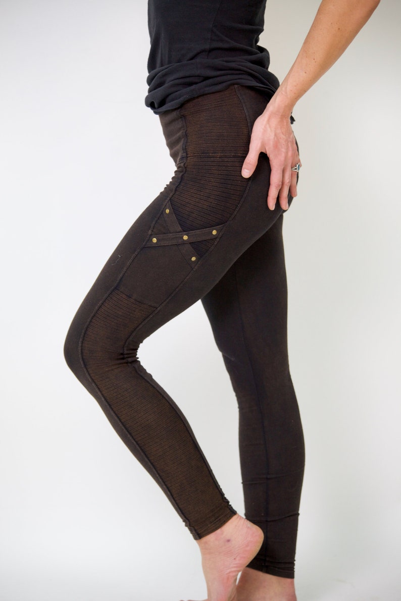 May include: Brown leggings with a decorative panel on the left thigh featuring a criss-cross design and gold-toned studs.