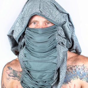 May include: A person wearing a grey hooded garment with a geometric pattern. The hood is pulled up over their head, covering their face except for their eyes. The garment has a gathered, pleated effect around the neck.