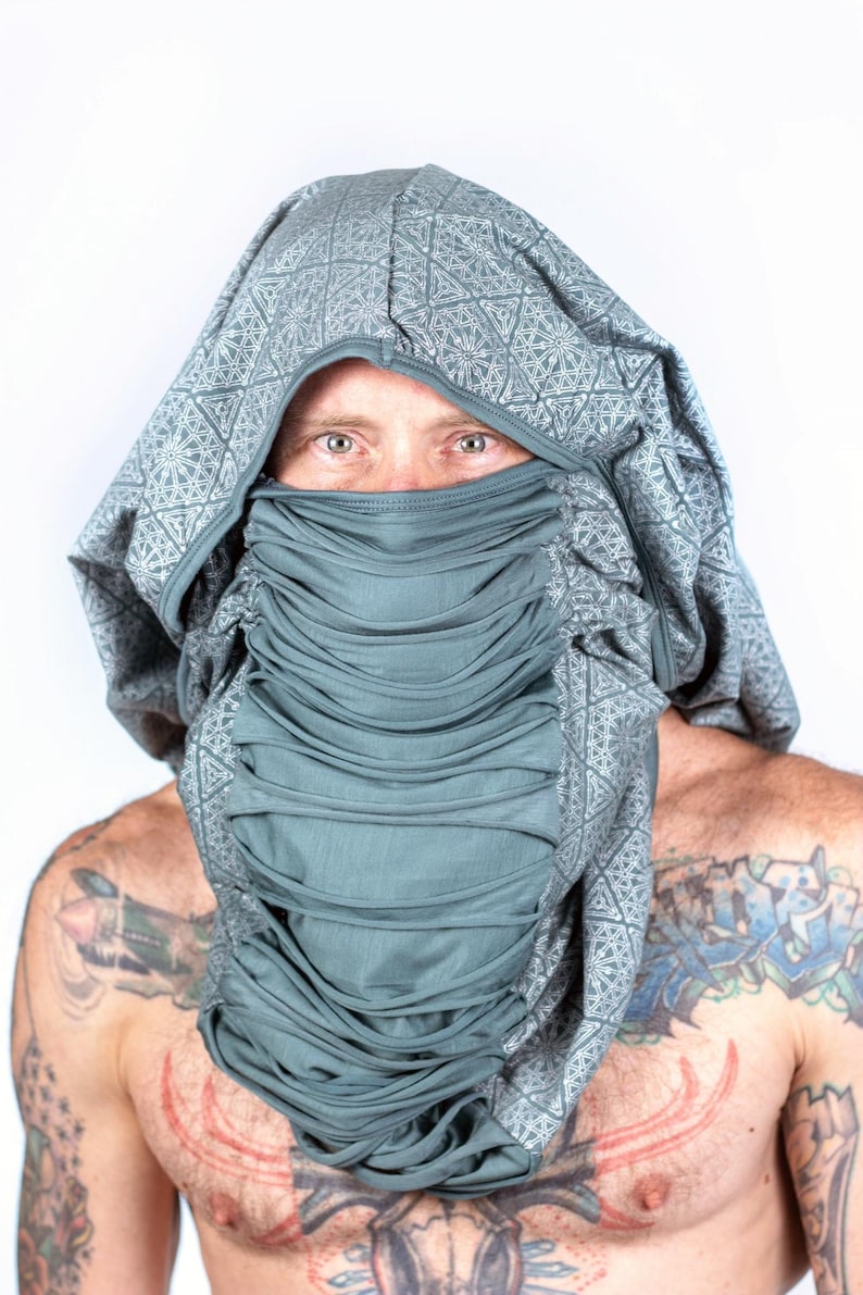 May include: A person wearing a grey hooded garment with a geometric pattern. The hood is pulled up over their head, covering their face except for their eyes. The garment has a gathered, pleated effect around the neck.