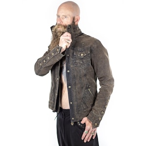 May include: A distressed brown denim jacket with button details, a high collar, and multiple pockets. The jacket has a vintage, worn look and is paired with black pants. The style is reminiscent of steampunk or alternative fashion.