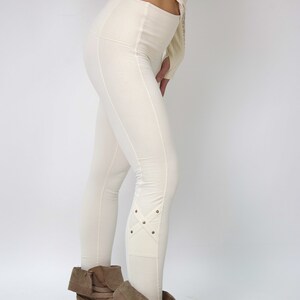 May include: White leggings with a textured design and decorative stitching on the lower legs. The leggings are paired with brown ankle boots.