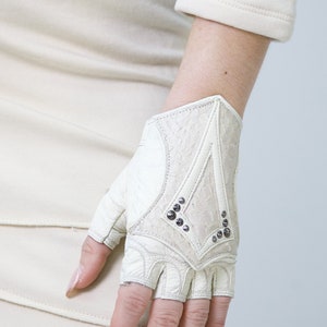 K&ouml;nnte beinhalten: Wei&szlig;e fingerlose Lederhandschuhe mit einem dekorativen Design und silbernen Nieten.