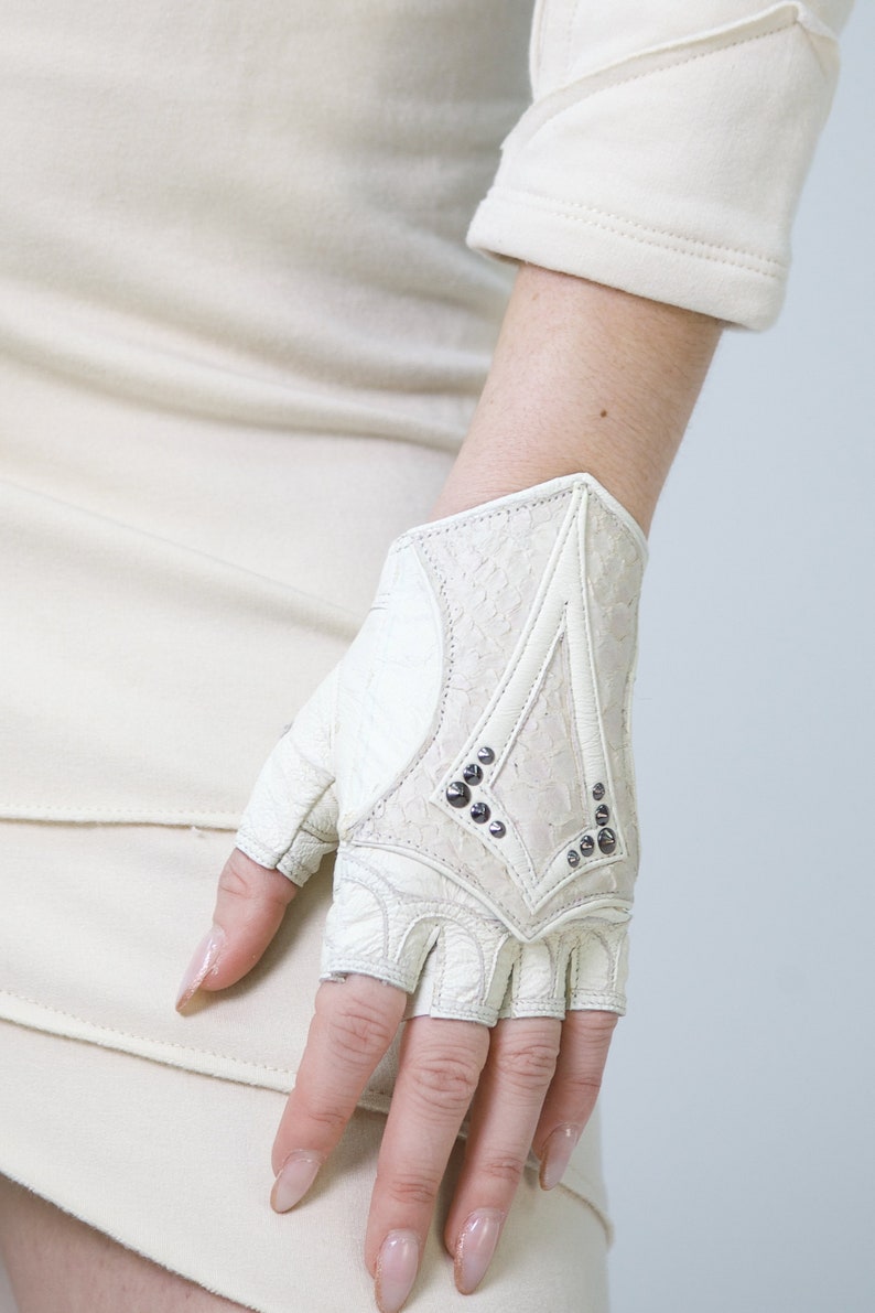 K&ouml;nnte beinhalten: Wei&szlig;e fingerlose Lederhandschuhe mit einem dekorativen Design und silbernen Nieten.