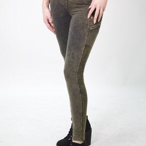 May include: A pair of dark green leggings with a distressed look and a zipped pocket on the right leg. The leggings have a high waist and are made of a soft, stretchy fabric.