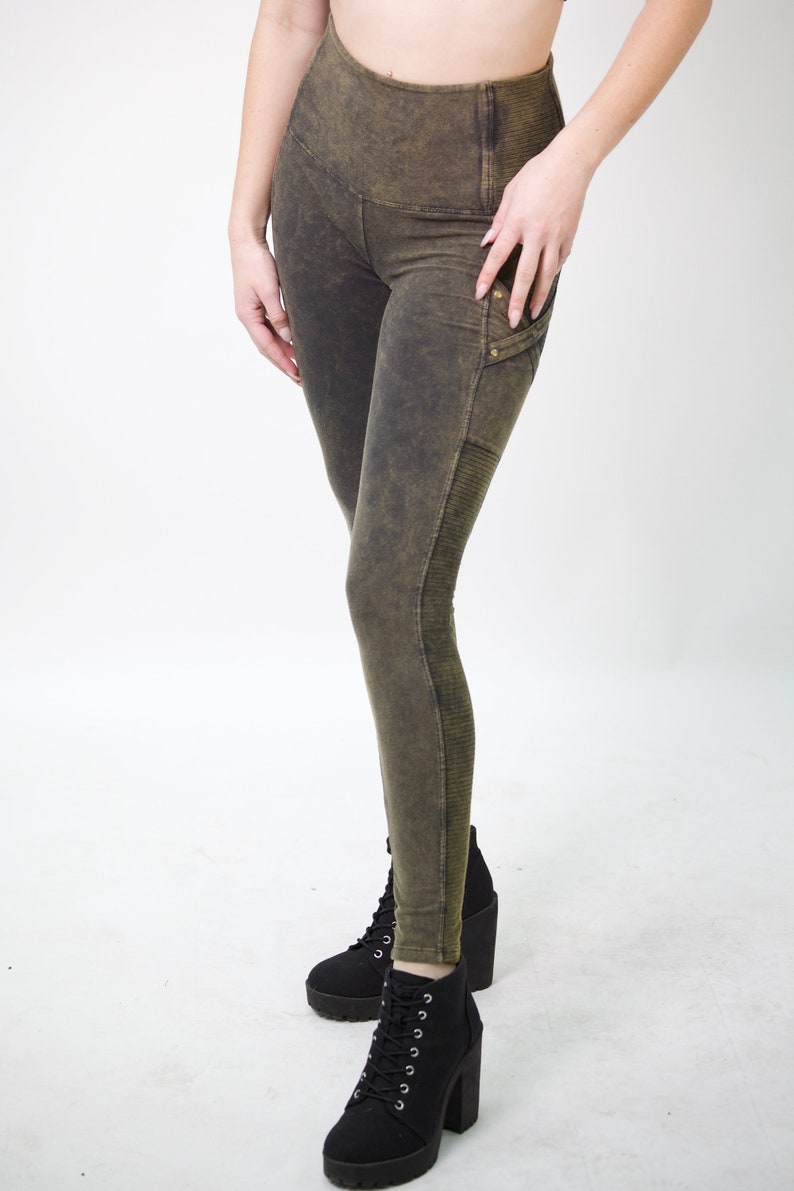May include: A pair of dark green leggings with a distressed look and a zipped pocket on the right leg. The leggings have a high waist and are made of a soft, stretchy fabric.