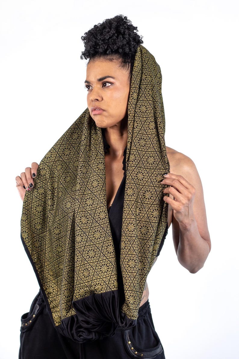 May include: A woman wearing a black and gold patterned scarf with a geometric design. The scarf is draped over her head and shoulders, and she is looking to the side.