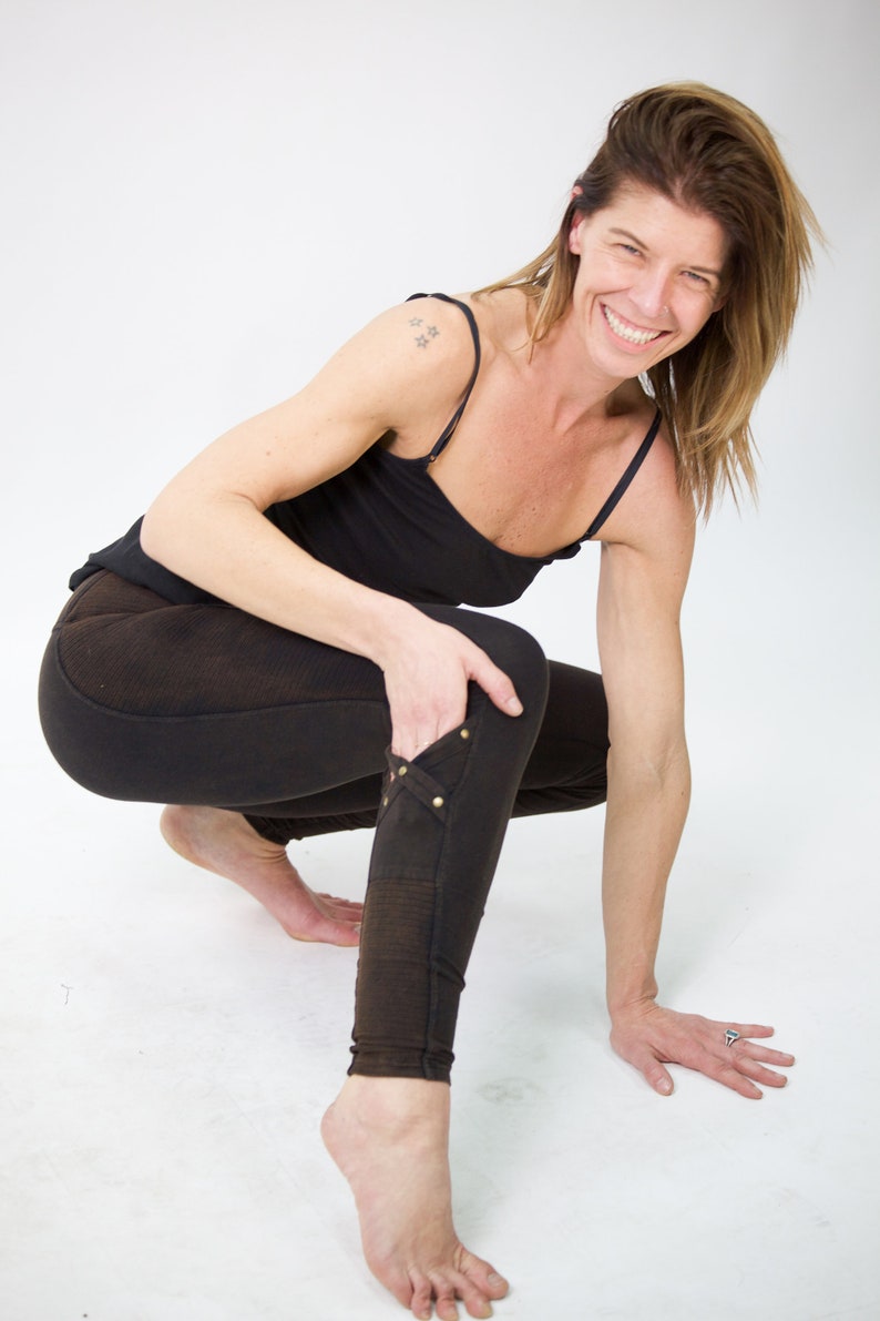 May include: A woman wearing black leggings with a decorative detail on the leg and a black tank top. She is crouching with her arms bent and her hands on the ground.
