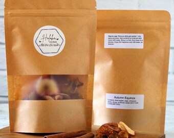 May include: Two brown paper pouches with clear windows, one labeled "Holoka Home" and the other "Autumn Equinox." Cinnamon sticks and dried spices sit on a wooden board. The text on the label says "NOT FOR CONSUMPTION."