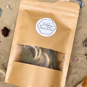 May include: A brown kraft paper stand-up pouch with a clear rectangular window and a white circular label featuring the text Hofoka HOME in a black script font, surrounded by a black hexagonal border and small green leaf illustrations.