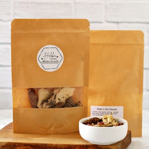 May include: Two brown paper bags with a white label that says "Holokai Home" on the front. The bags contain dried fruit and other natural ingredients. The bags are sitting on a wooden cutting board. A white bowl with dried fruit and other natural ingredients is in front of the bags. The bowl has a label that says "Walk in the Woods".