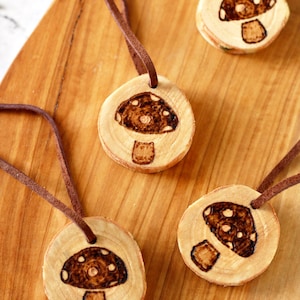 May include: Four wooden mushroom pendants with brown leather cords. Each pendant is a wood slice with a burned mushroom design.