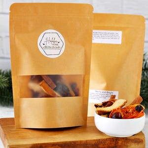 May include: Two brown paper bags with a clear window showing dried fruit and spices. A white bowl filled with dried fruit and spices sits on a wooden board. The bags have a white label with the text "Hofoka Home".