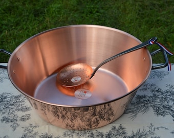 May include: A large copper pot with black handles and a copper ladle with a perforated bowl. The pot has a decorative design on the bottom.