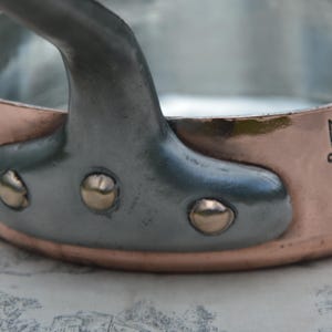 May include: A copper saucepan with a silver handle and a wolf logo that says "E. Staub & Sohn".