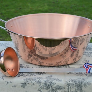 May include: A copper-colored, large, round bowl with two silver handles and a matching ladle. The bowl has a decorative black and white toile pattern around the exterior. Red, white, and blue ribbons are tied to the handles and ladle.