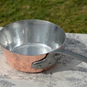 May include: A copper saucepan with a silver handle. The saucepan has a hammered finish and is suitable for cooking on the hob.