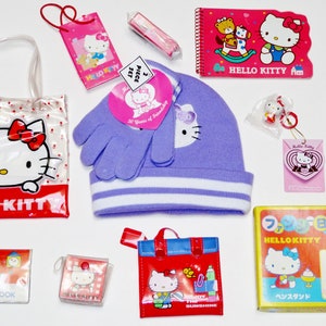 May include: A collection of Hello Kitty themed merchandise. Items include a clear tote bag, a purple beanie and gloves set, a notepad, a pencil, a keychain, and various small bags and accessories, all featuring the iconic character.
