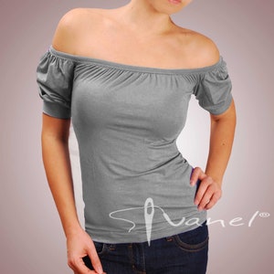 May include: A gray off-the-shoulder top with short sleeves and a fitted silhouette. The top has a small white logo on the front that says "Svanel".