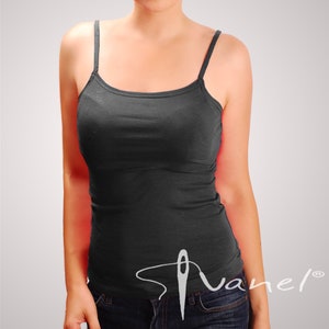 Könnte beinhalten: Ein schwarzes Tanktop mit dünnen Trägern. Das Tanktop ist aus weichem, dehnbarem Stoff. Das Tanktop wird auf einem Model gezeigt, das eine blaue Jeans trägt.