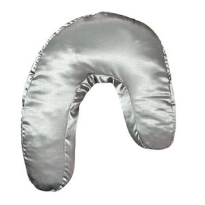 May include: A silver satin U-shaped pillow. The pillow is designed to provide support for the neck and head.