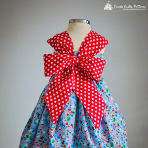 May include: A blue and red Christmas-themed dress with a large red bow on the back. The dress has a white polka dot pattern on the bow and a red polka dot trim around the bottom.