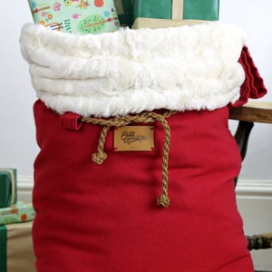 May include: Red Santa sack with a white faux fur trim and a brown rope drawstring. The sack has a brown leather label that says "Santa's Workshop London".