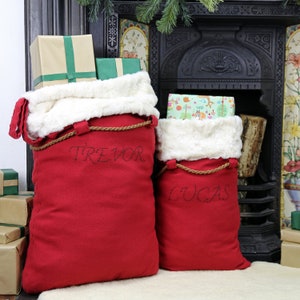 May include: Two red Santa sacks with white faux fur trim and brown rope handles. The sacks are personalized with the names "Trevor" and "Lucas".