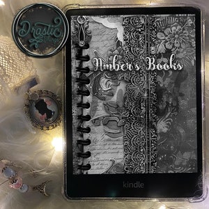 Puede incluir: Un lector electrónico Kindle en blanco y negro con una cubierta decorativa que dice "Amber's Books" y "kindle". La cubierta tiene un diseño floral y un aspecto vintage.