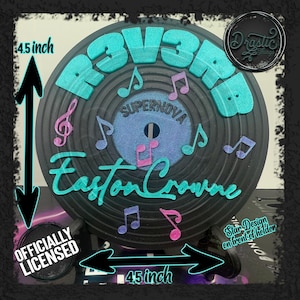 Peut inclure: Un objet décoratif rond noir avec le texte "R3V3R" en turquoise et "Easton Crowne" en écriture turquoise. Le centre présente "SUPERNOVA" et des notes de musique. La pièce mesure 11,4 cm de diamètre et est officiellement licenciée.