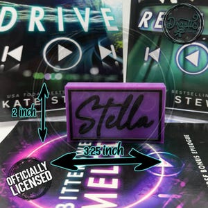 May include: A rectangular, purple Stella nameplate, 3.25 inches wide and 2 inches tall, with black lettering. The nameplate is set against a background of book covers. The image includes the text "Officially Licensed."