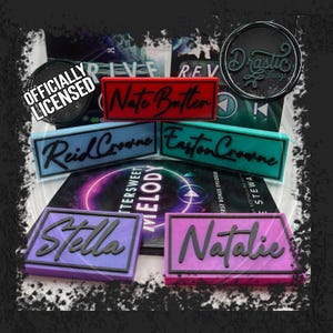 Peut inclure: Plusieurs étiquettes rectangulaires de différentes couleurs, dont le rouge, le bleu et le violet, avec des lettres noires. Les étiquettes comportent des noms tels que "Nate Butter" et "Stella". L'image comprend également un badge circulaire "Officially Licensed".