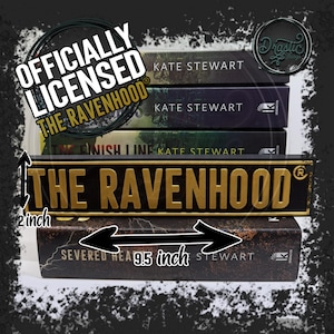 Puede incluir: Una pila de libros y un letrero con el texto "THE RAVENHOOD". El letrero mide 24 cm de largo y 5 cm de alto. Los libros son de Kate Stewart. La imagen también incluye el texto "OFFICIALLY LICENSED THE RAVENHOOD".