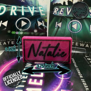 May include: A pink rectangular nameplate, 3.75 inches wide and 2 inches tall, with the name "Natalie" in black script. The nameplate is placed on top of a book with the word "DRIVE" visible. The words "OFFICIALLY LICENSED" are also visible.