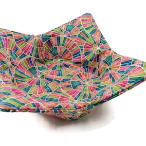 May include: A colorful bowl cozy with a geometric pattern of pink, green, and blue circles. The cozy is made of fabric and has a quilted texture.