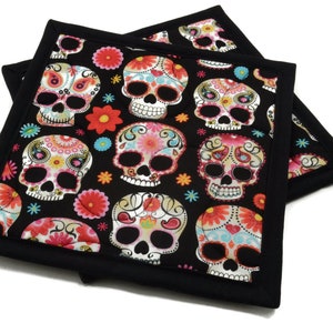 May include: Two black quilted pot holders with a colorful sugar skull pattern. The skulls are decorated with pink, blue, yellow, and white details.