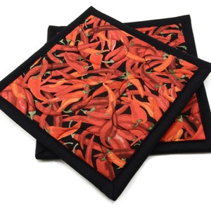May include: Two red and black quilted hot pads with a chili pepper pattern. The hot pads are made of fabric and have a black border.
