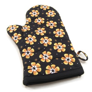 May include: Black oven mitt with a quilted design featuring orange and white candy corn flowers.