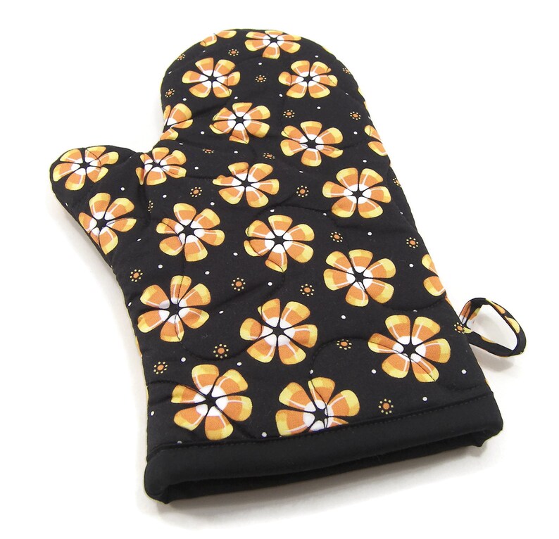 May include: Black oven mitt with a quilted design featuring orange and white candy corn flowers.