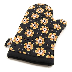 May include: Black oven mitt with a pattern of orange and white candy corn flowers. The mitt has a quilted texture and a hanging loop.