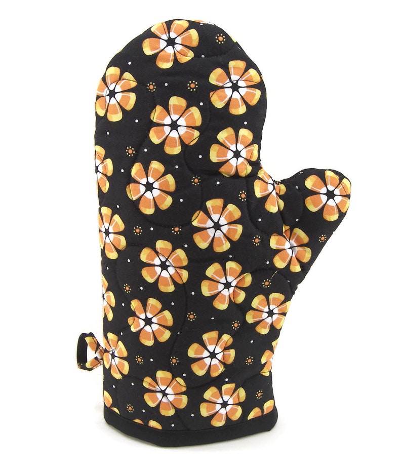 May include: Black oven mitt with a pattern of orange and white candy corn flowers.