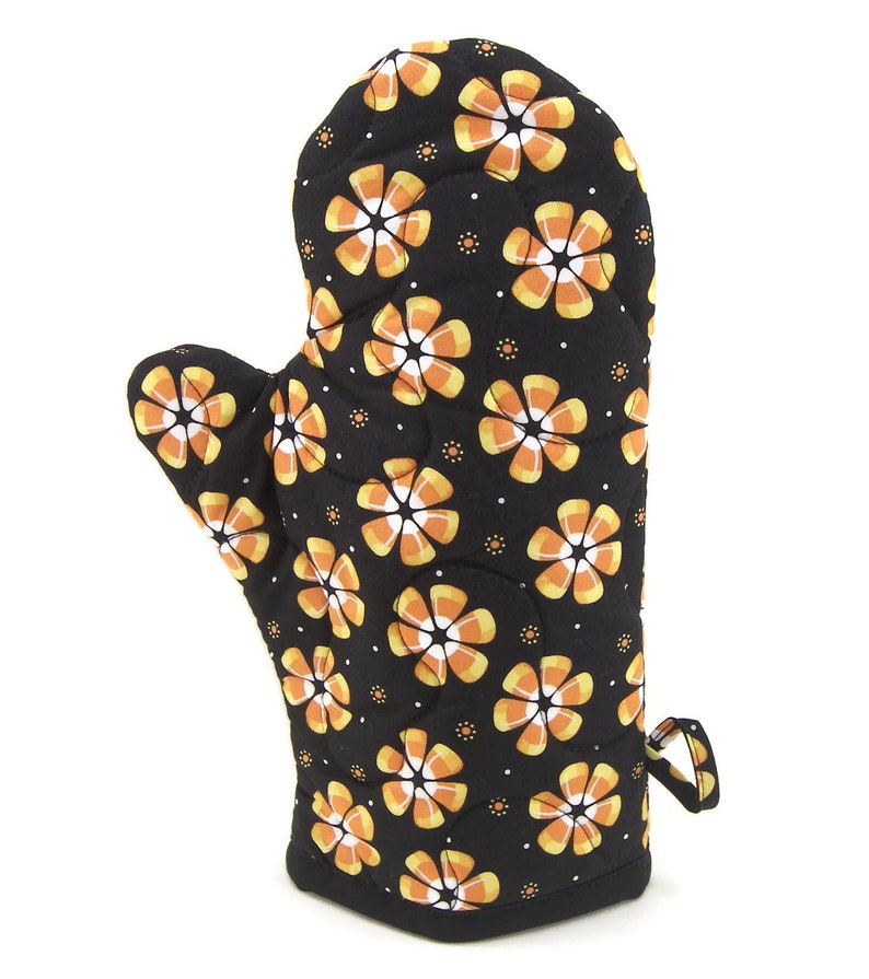 May include: Black oven mitt with a pattern of orange and white candy corn flowers.