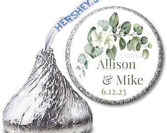 May include: A silver foil-wrapped Hershey's Kiss with a custom sticker. The sticker has a floral design with white flowers and green leaves, and the names "Allison & Mike" with the date "6.12.23". The Hershey's Kiss wrapper has the word "HERSHEY'S" on the paper strip.