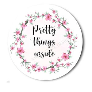 May include: A round white sticker with the words "Pretty things inside" in black script. The text is surrounded by a watercolor floral wreath of pink blossoms and green leaves.