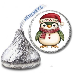 May include: A Hershey's Kiss candy with a silver foil wrapper next to a circular graphic of a cartoon penguin wearing a Santa hat and a red scarf. The penguin has a white belly and green wings.