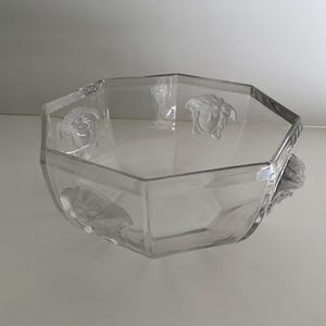 Puede incluir: Cuenco de vidrio transparente, octogonal, con detalles en relieve de cabeza de Medusa. El cuenco tiene un dise&ntilde;o geom&eacute;trico y probablemente se utiliza con fines decorativos o de servicio. El vidrio transparente permite ver el contenido.